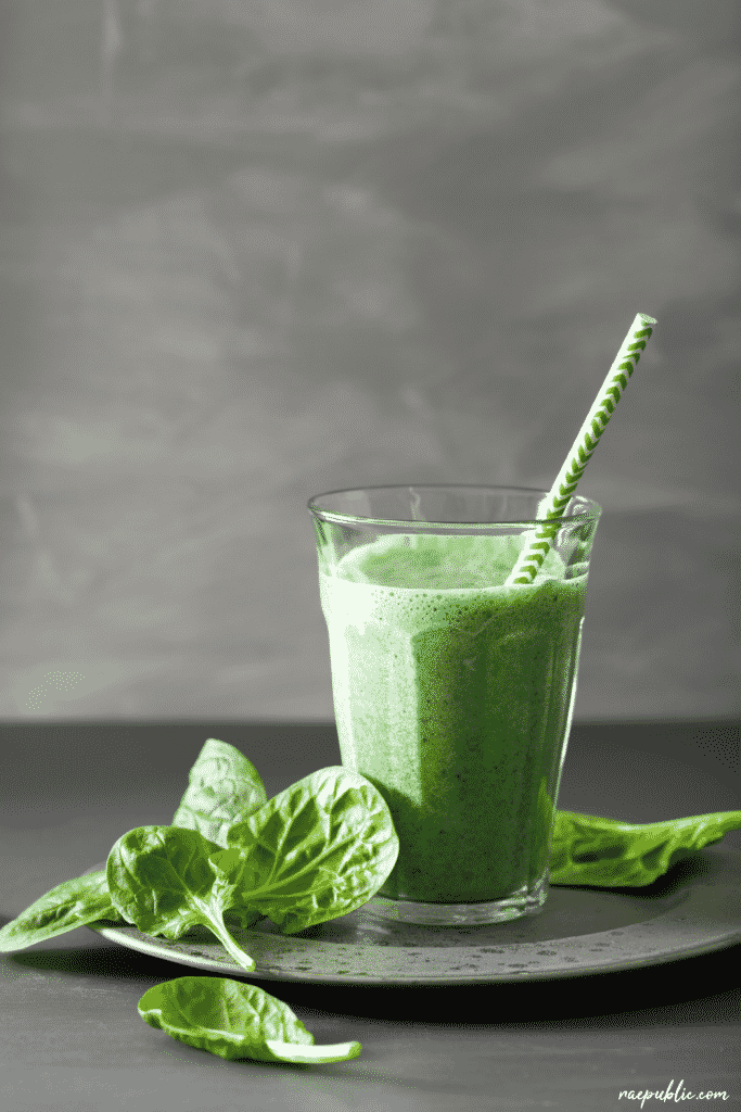 Cup of green smoothie with fresh spinach on the side.
