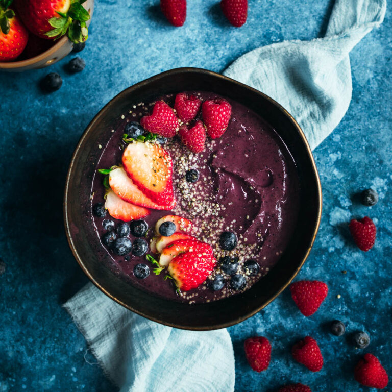 A bowl of acai blueberry smoothie with berries and hemp seeds on a blue background.