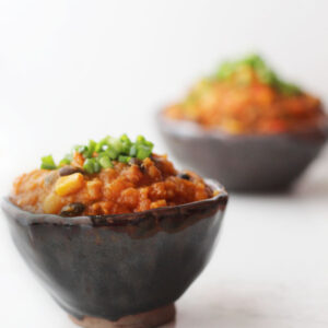 Two bowls of pumpkin chili with green onions on top.