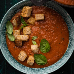 Bowl of vegan tomato soup with fresh basil and croutons on top.