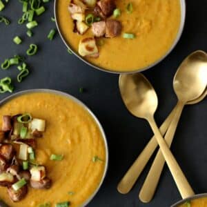 Two bowls of peanut carrot soup with gold spoons on the side.
