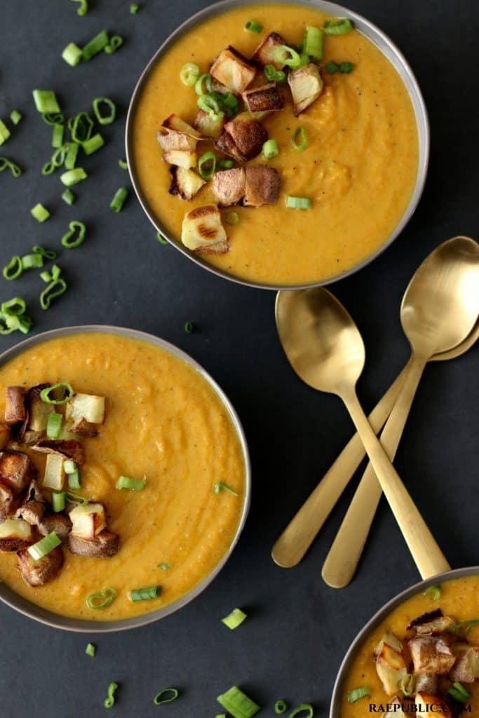 Two bowls of peanut carrot soup with gold spoons on the side. 
