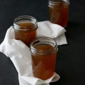 Clear glass mason jars filled with veggie broth on a white cloth napkin.