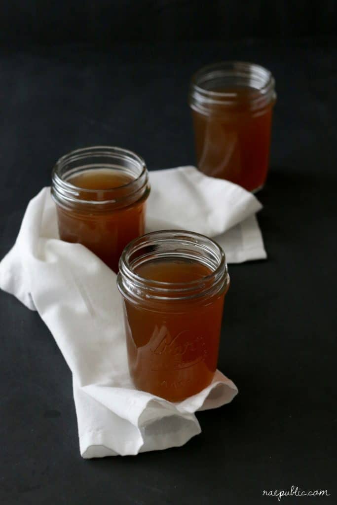 Clear glass mason jars filled with veggie broth on a white cloth napkin.
