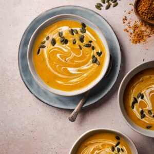 Three bowls of creamy soup with pumpkin seeds and fall leaves.