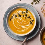 Three bowls of creamy soup with pumpkin seeds and fall leaves.