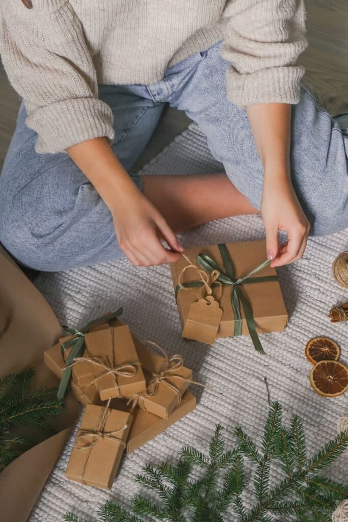 Woman wrapping gifts in kraft paper, tied with fabric ribbon.
