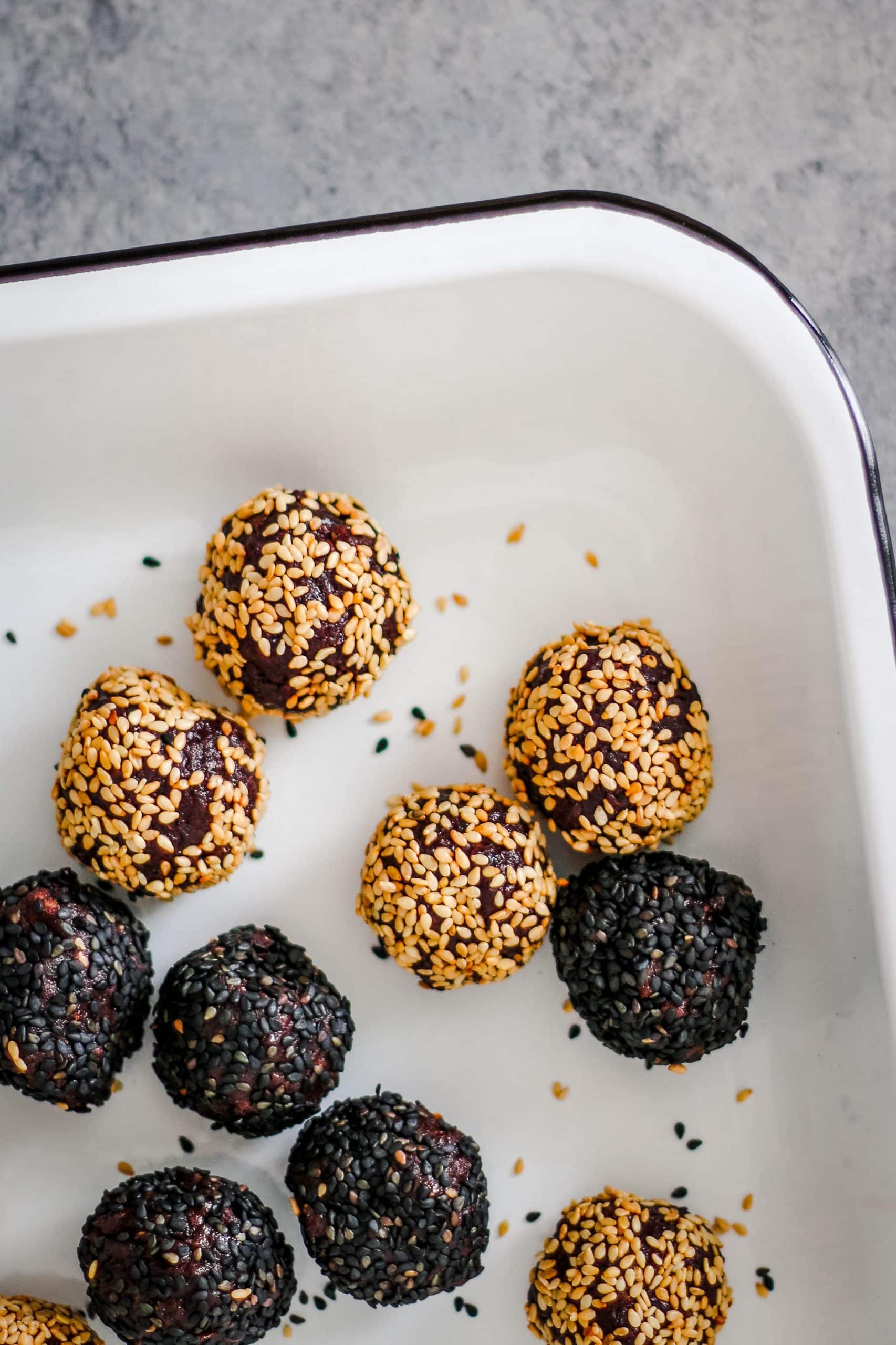 Sesame coated date balls on an enamel tray.
