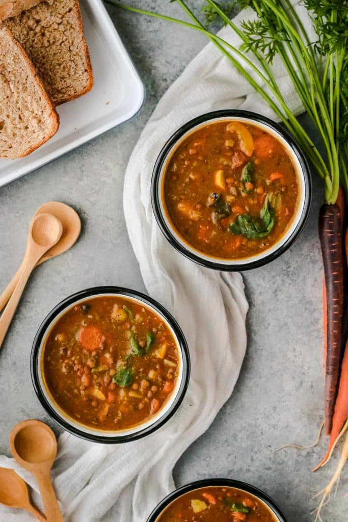 Two bowls of lentil veggie soup on a tray with bread.