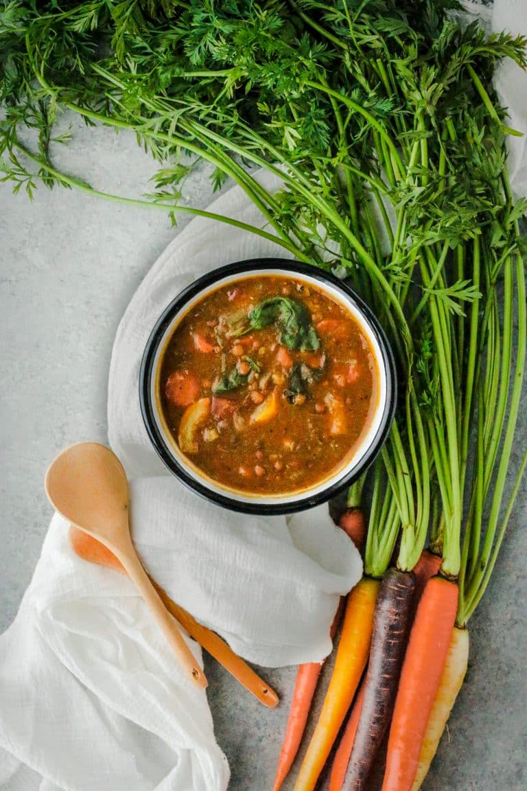 One enamel bowl of lentil soup with rainbow carrots next to it.