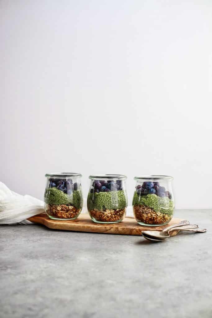 Layered jar of granola, green chia pudding, blueberries, and chocolate.