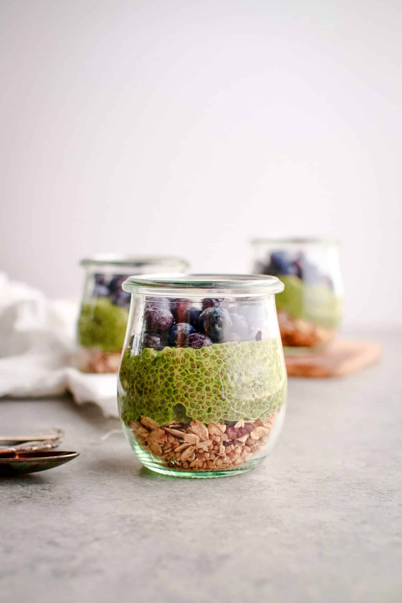 Layered jar of granola, green chia pudding, blueberries, and chocolate.