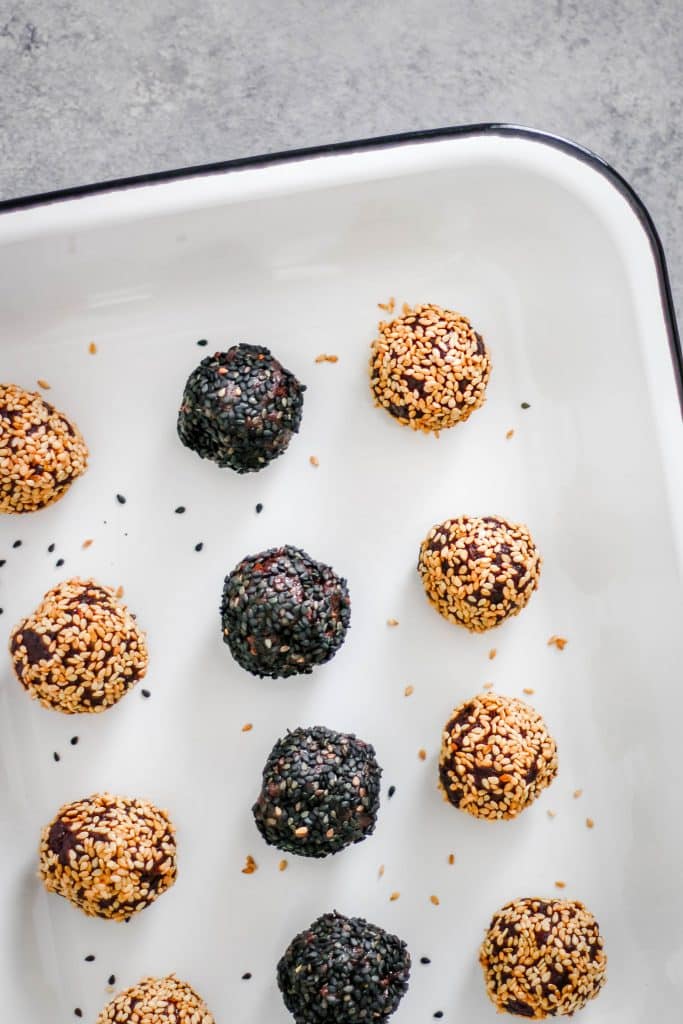 Enamel tray with chocolate tahini date balls in rows of black sesame and toasted sesame.