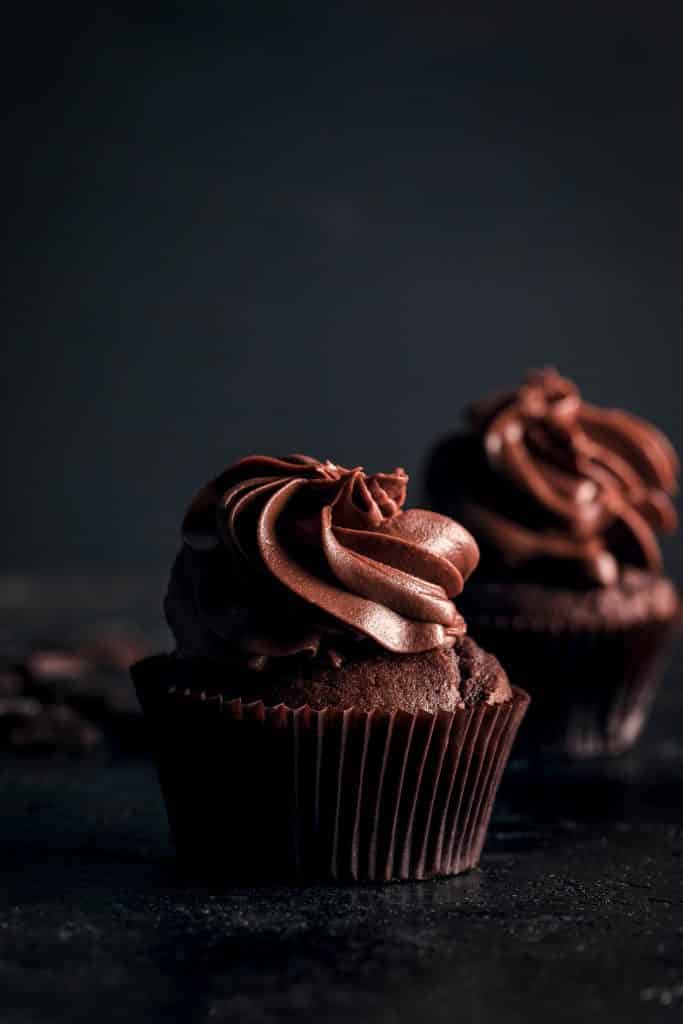 Two vegan chocolate cupcakes on a black surface.