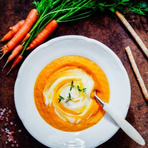 Bowl of healthy carrot ginger soup with bread sticks and a bunch of carrots.