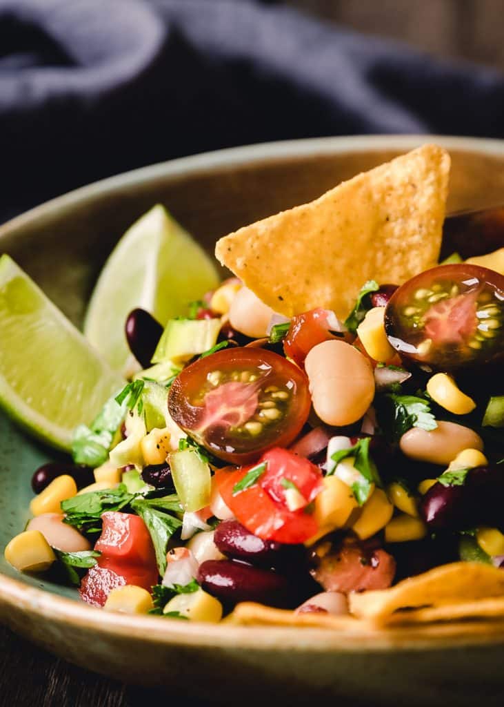 Bowl of bean salad with lime wedges and tortilla chips.