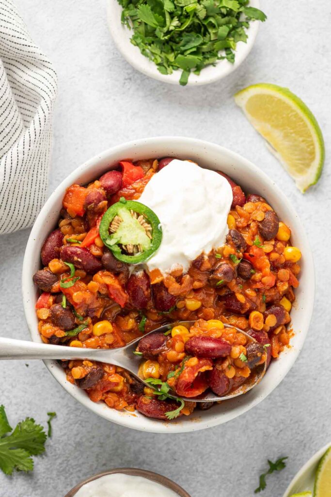 Bowl of red lentil chili with sliced jalapeño and vegan sour cream on top.