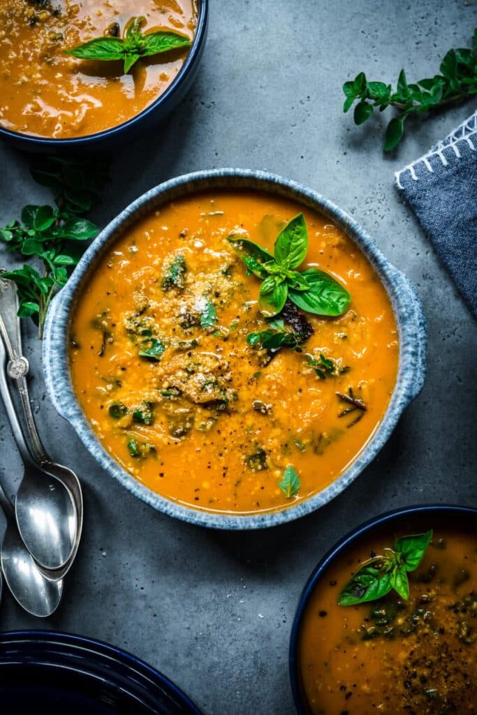 Large bowl of deep orange colored squash soup with basil on top.
