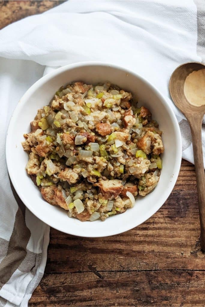 Large bowl of vegan stuffing on a wooden table and a white cloth napkin.