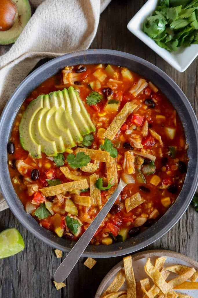 Large bowl of tortilla soup with tortilla strips and avocado on top.
