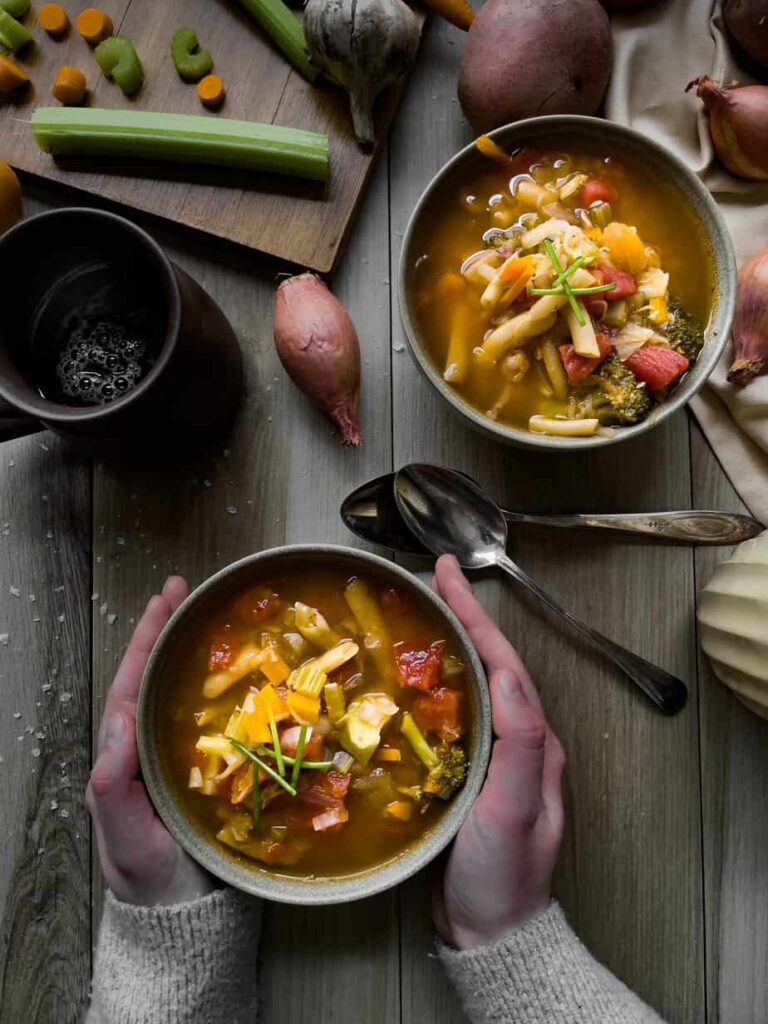 Two bowls of veggie soup with woman holding one bowl. 