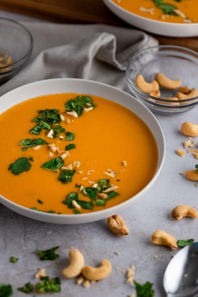 Large bowl of orange colored soup with fresh green herbs on top.