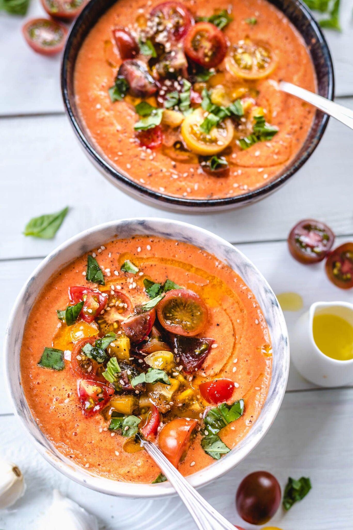 Two bowls filled with orange colored cold soup topped with sliced tomatoes and herbs.
