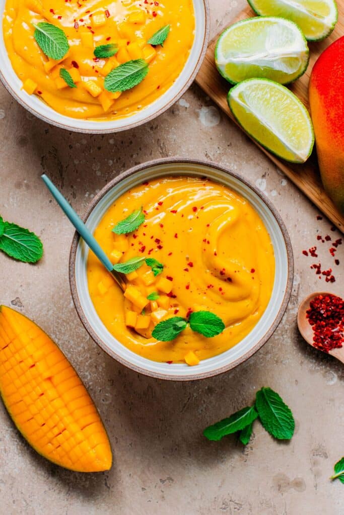 Two bowls of orange colored cold soup topped with fresh herb. 