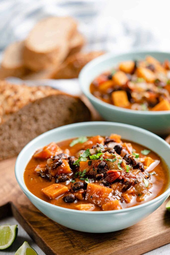 Two bowls of sweet potato black bean soup with fresh bread next to it.