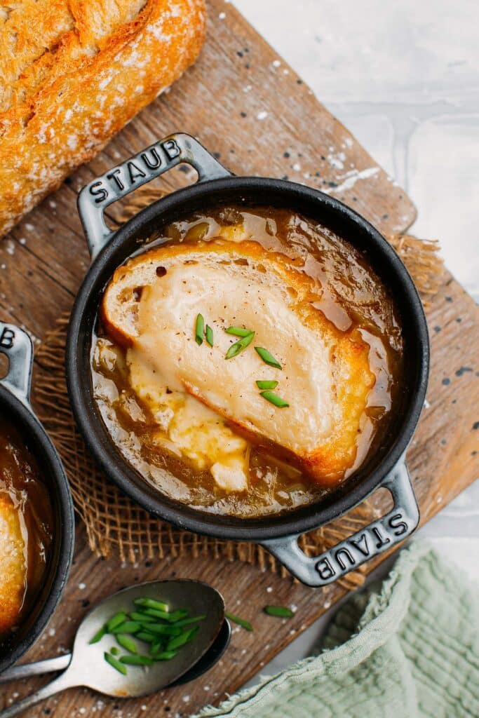 Gray Staub cocotte filled to the brim with French onion soup and toast topped with melted cheese. 