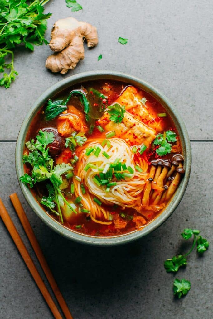 Large bowl of kimchi noodle soup topped with greens.