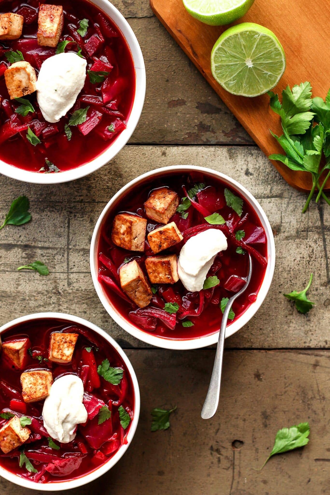 Three bowls of the BEST vegan beet soup with sour cream and lime.