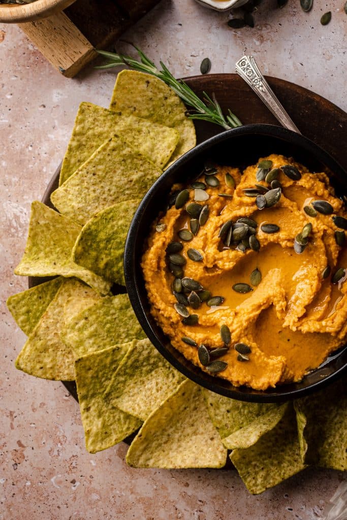 Black bowl of pumpkin hummus with olive oil drizzled on top.
