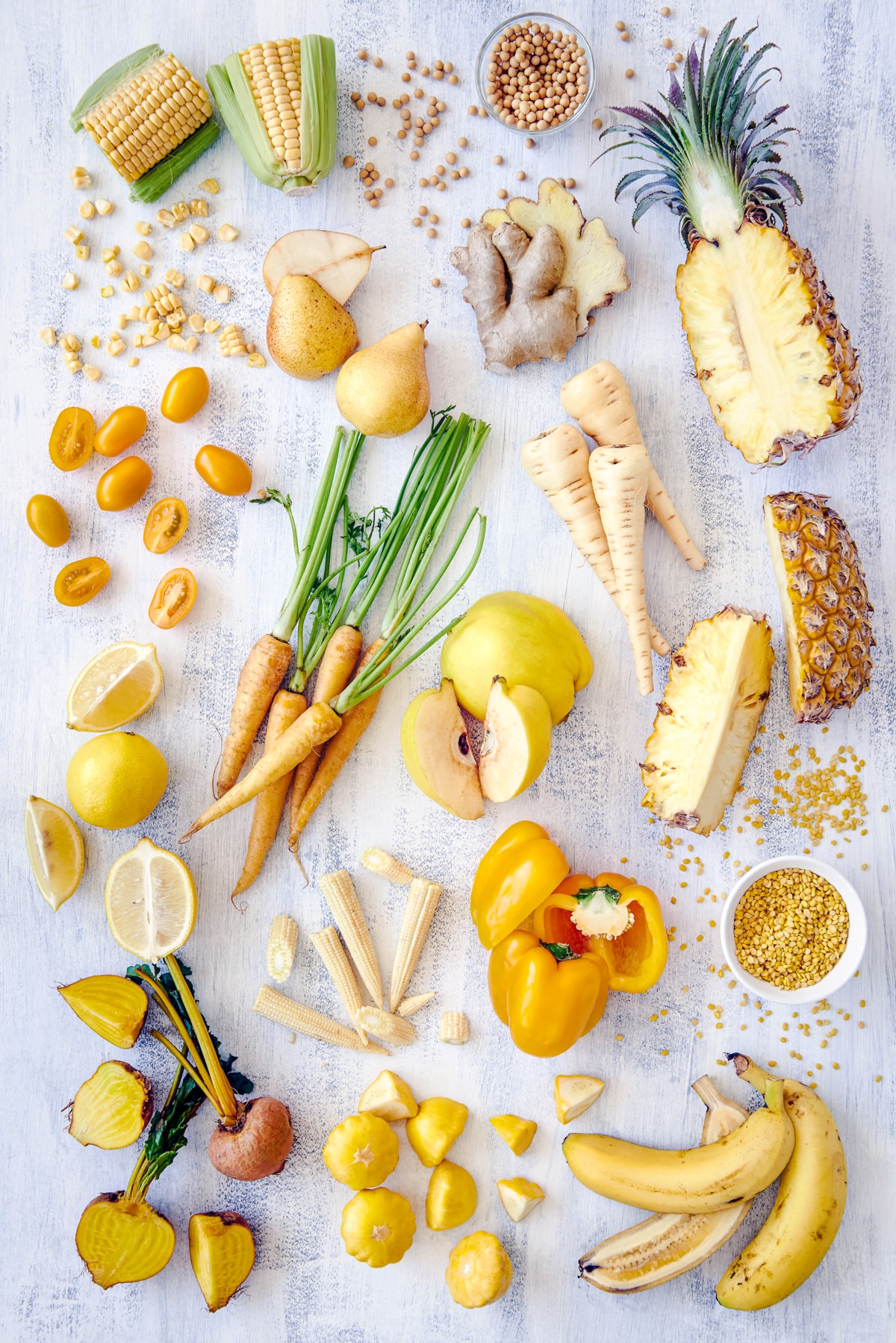 Many yellow fruits and veggies on a white surface.