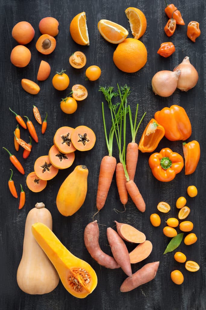 Butternut squash, carrots, oranges, and other orange fruits and vegetables on a black surface.