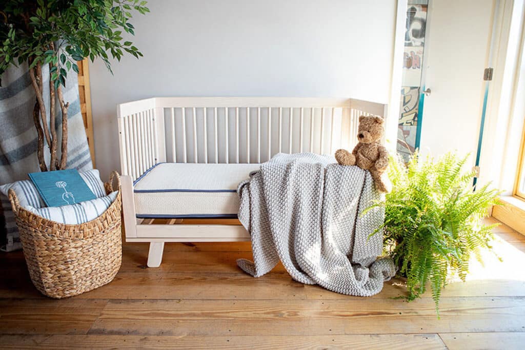 Organic crib mattress in wooden crib with gray blanket.