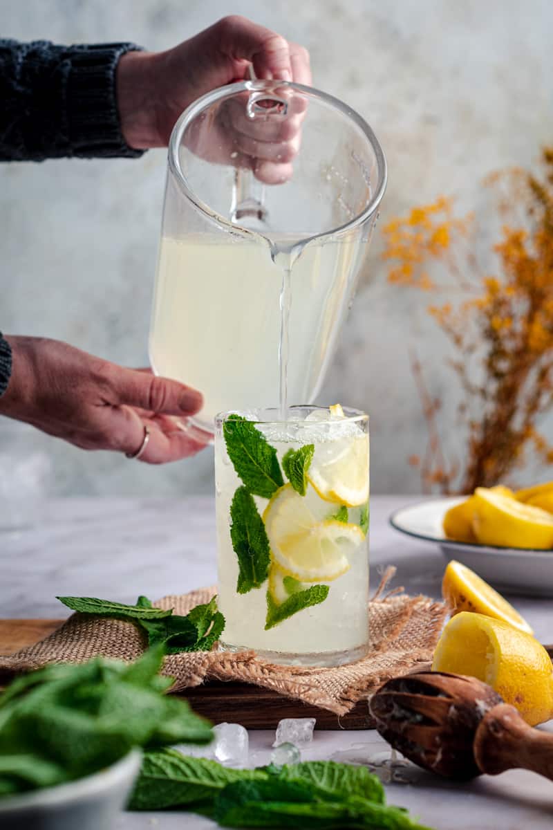 Pouring fresh lemonade into a glass with ices, mint, and lemon slices.