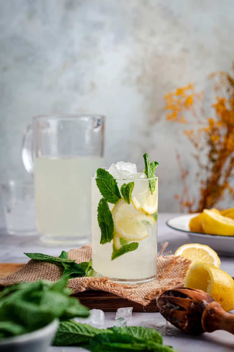 Glass and pitcher of lemonade with fresh mint and lemons around.
