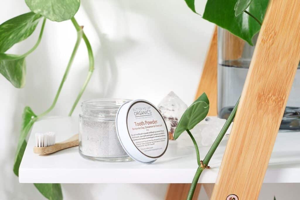 Glass jar of zero-waste toothpaste powder on a white shelf with a house plant.
