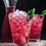 Up close of two cups and a pitcher of cranberry lemonade with fresh mint sprigs.