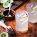 Limeade in two glass cups with ice and lime wedges.