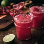 Two cups of pomegranate limeade with sliced limes around them.
