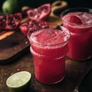 Two cups of pomegranate limeade with sliced limes around them.