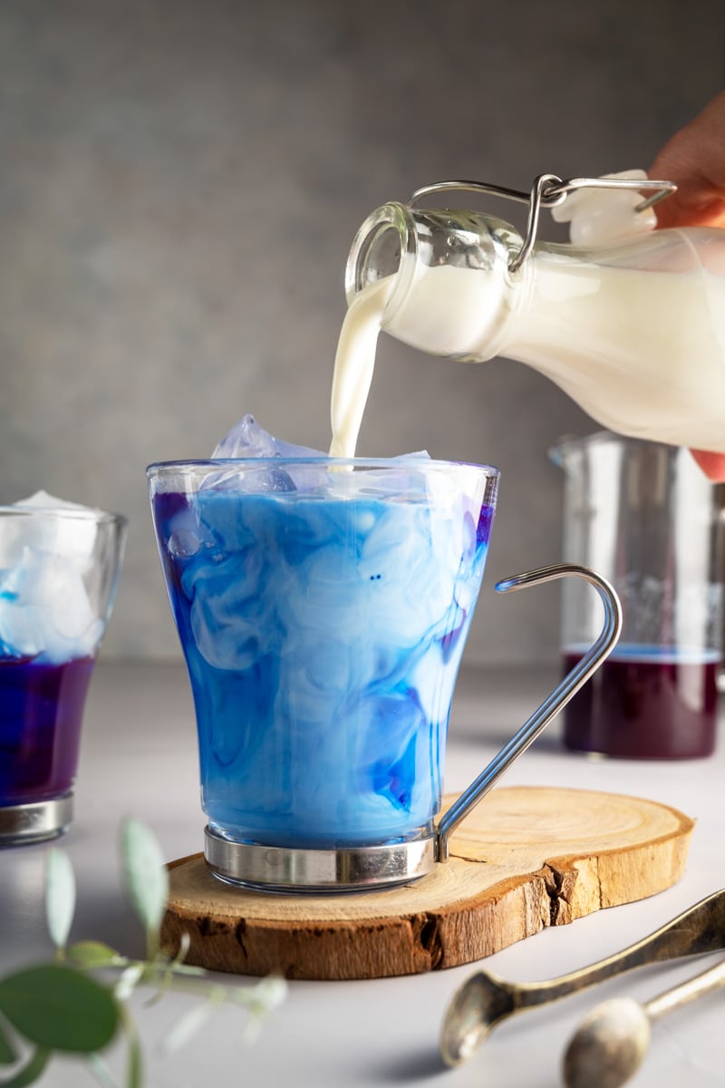 Bright blue butterfly pea flower latte in a clear glass cup.