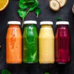 Four glass bottles filled with different veggie smoothies.