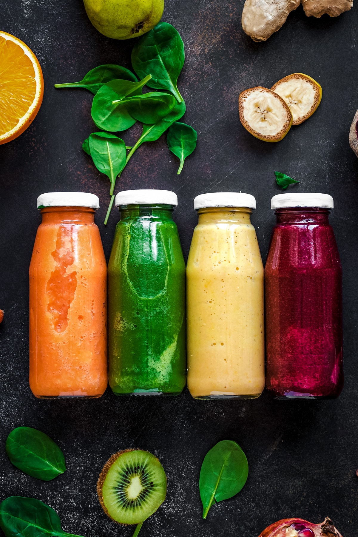 Four glass bottles filled with different veggie smoothies.