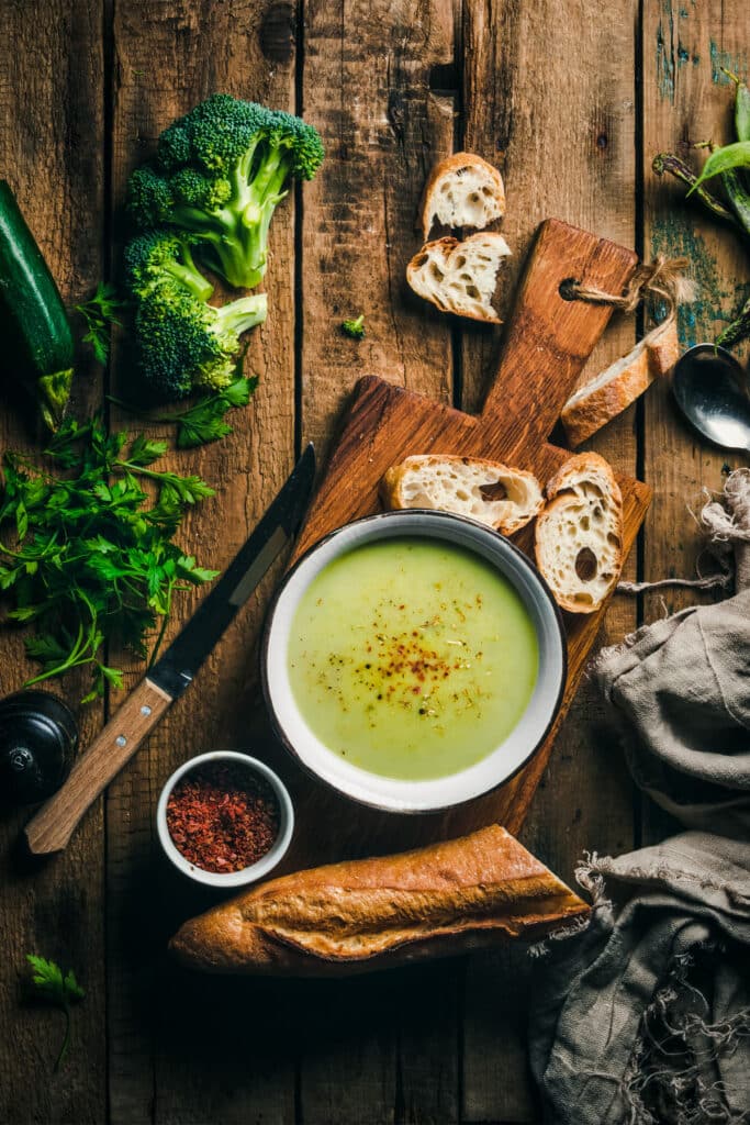 Bowl of green soup on a wooden board with fresh broccoli around.