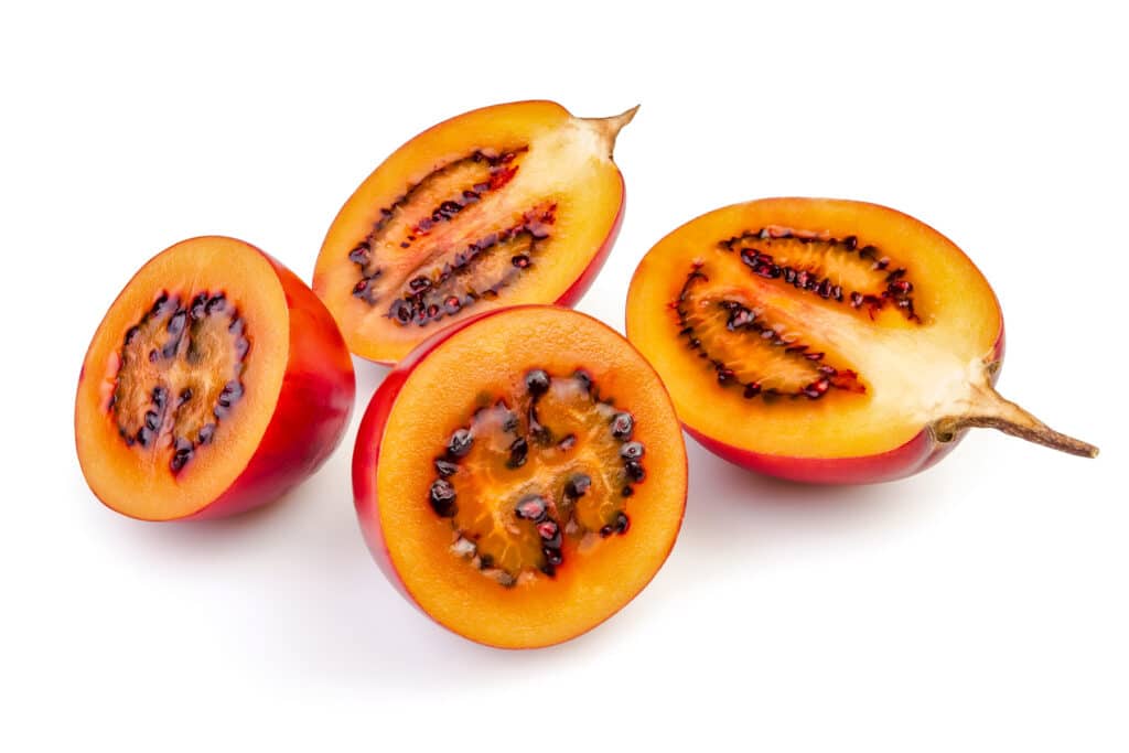 Two tamarillos cut in half showing their red to orange to yellow flesh. 