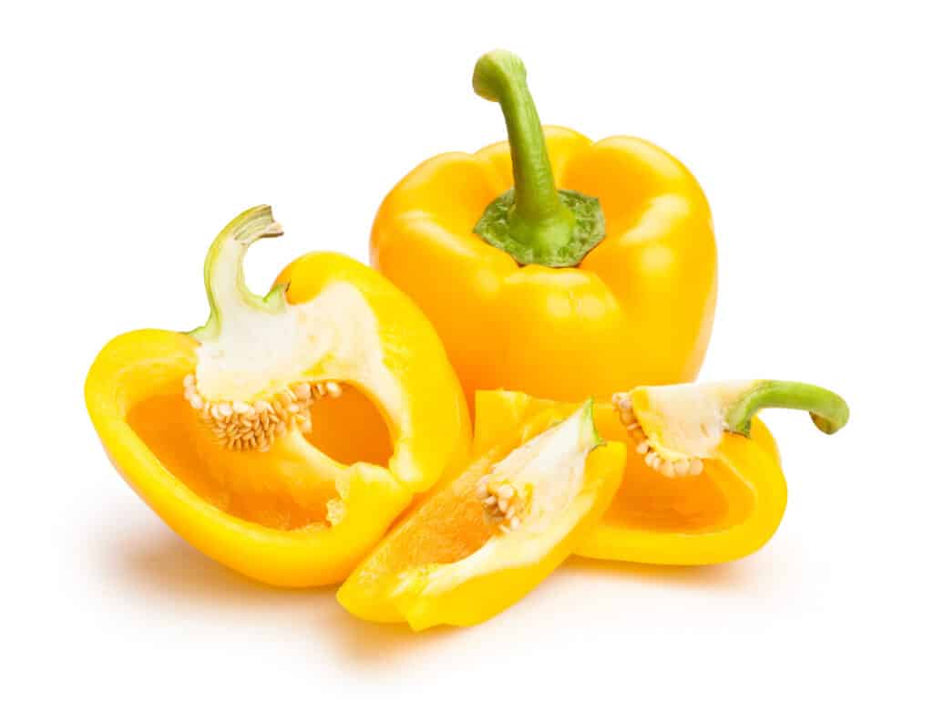 Two yellow colored bell peppers with one cut into slices showing its seeds.
