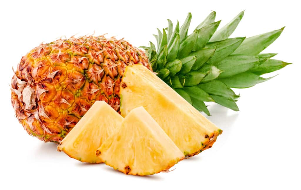 Traditional tan-yellow pineapple with a green top. Three slices of pineapple in front.